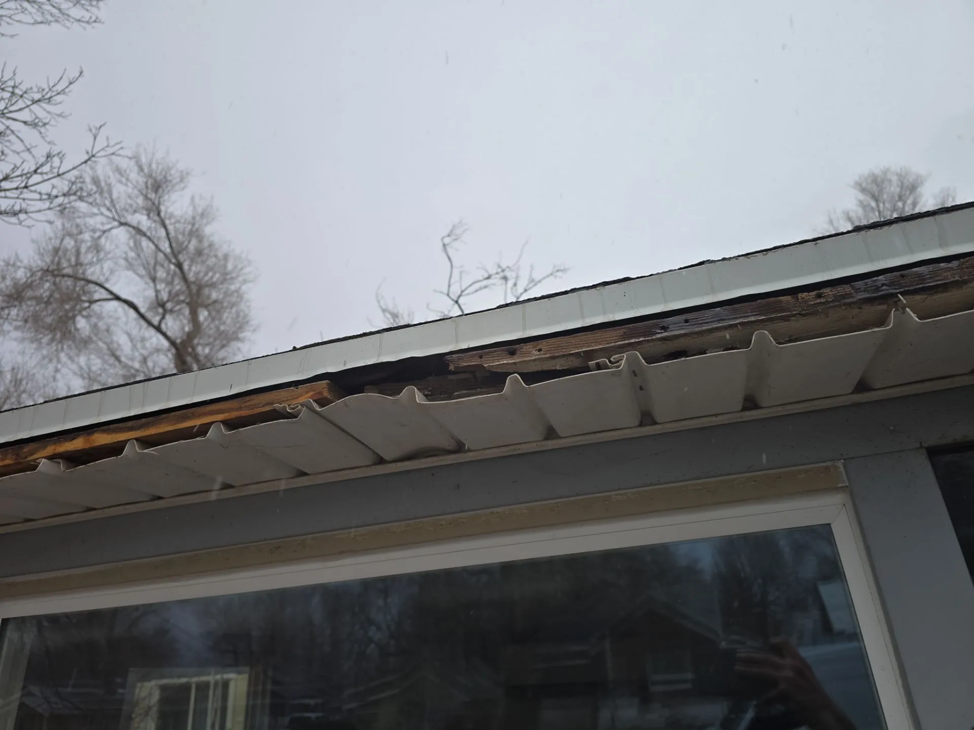 Damaged wood fascia and warped soffit beneath a roof edge