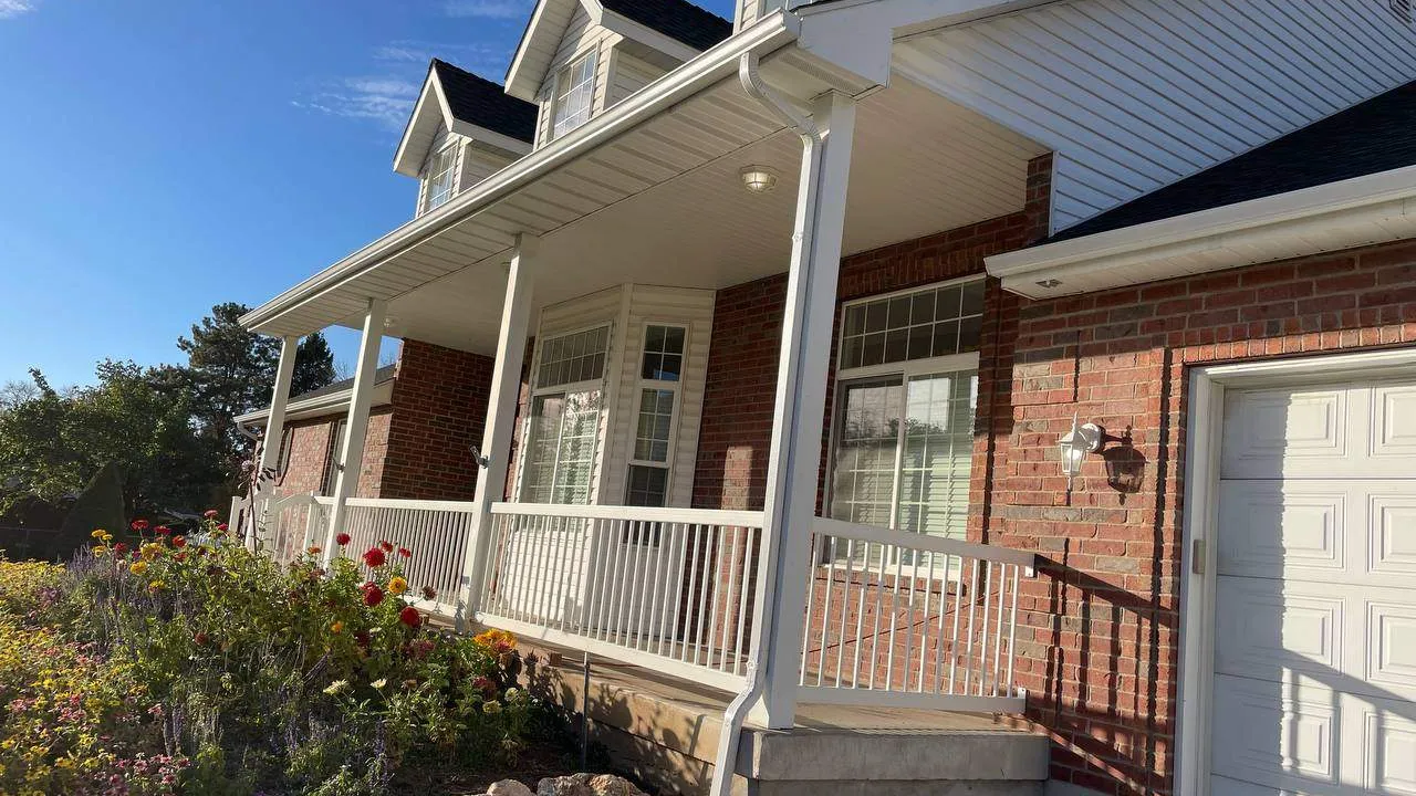 A brick-and-white home with white gutters and a downspout along the front porch